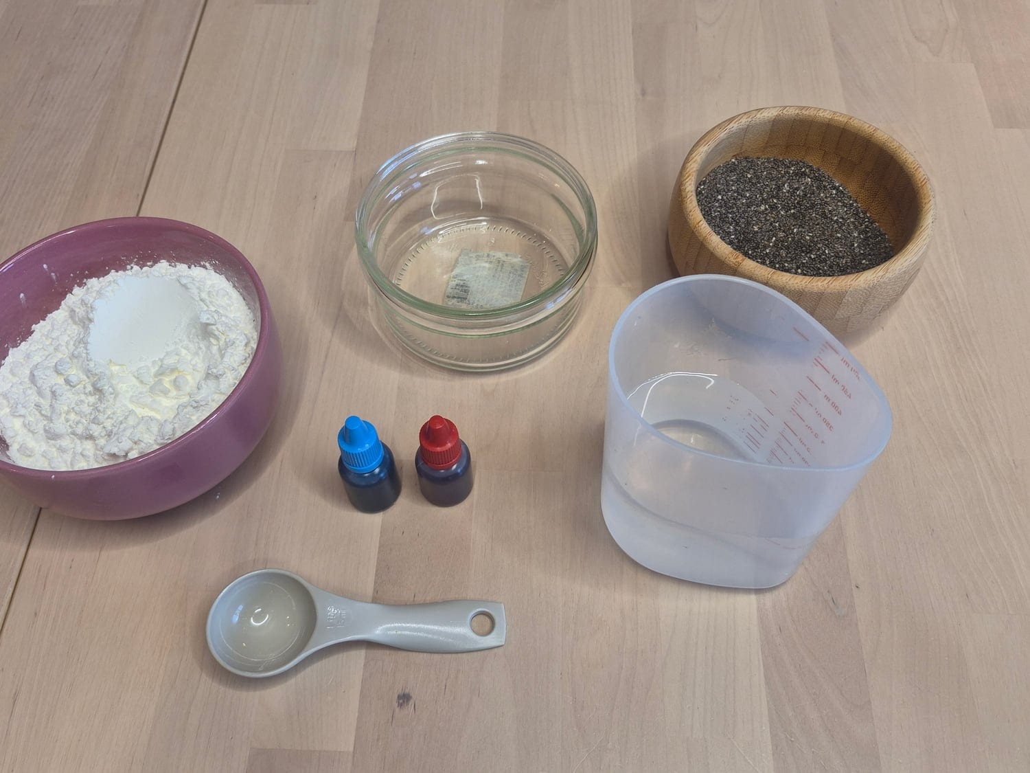 Frog-spawn potion materials: a bowl of cornstarch, a bowl of chia seeds, a glass bowl and a jug of water, blue and red food colouring and a measuring spoon