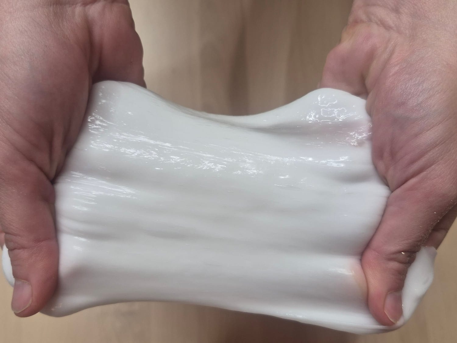 Two hands stretching thick white ghost slime into a wide, glossy band