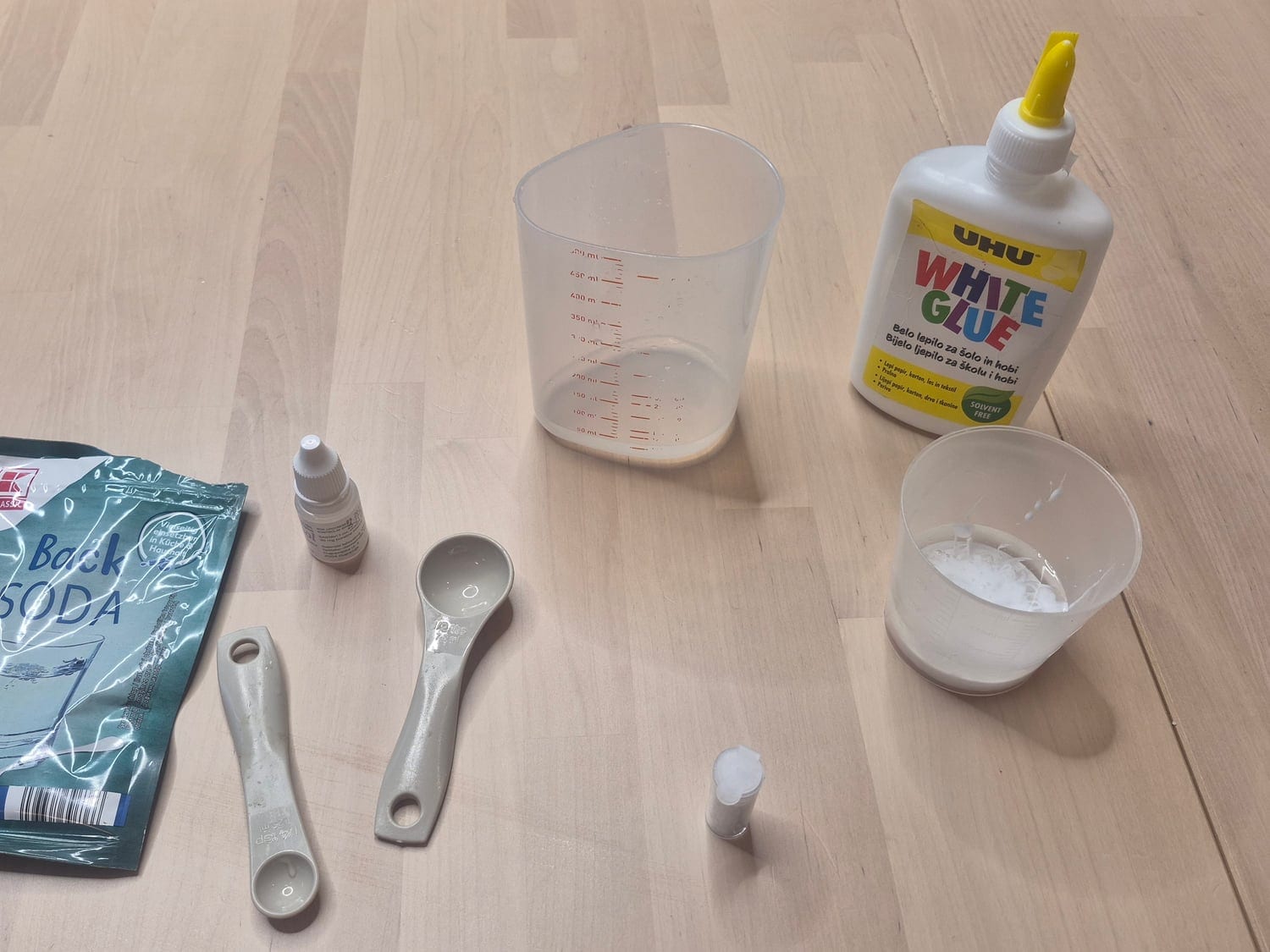 Ghost slime materials: white PVA glue, a sachet of baking soda, a small bottle of contact lens solution, a measuring cup of water and measuring spoons
