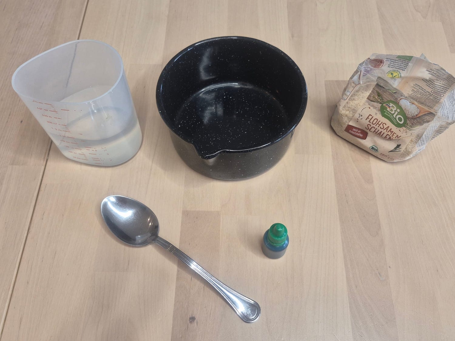 Monster snot materials: a bag of psyllium husk, a measuring cup of water, a small black pot, a spoon and green food colouring