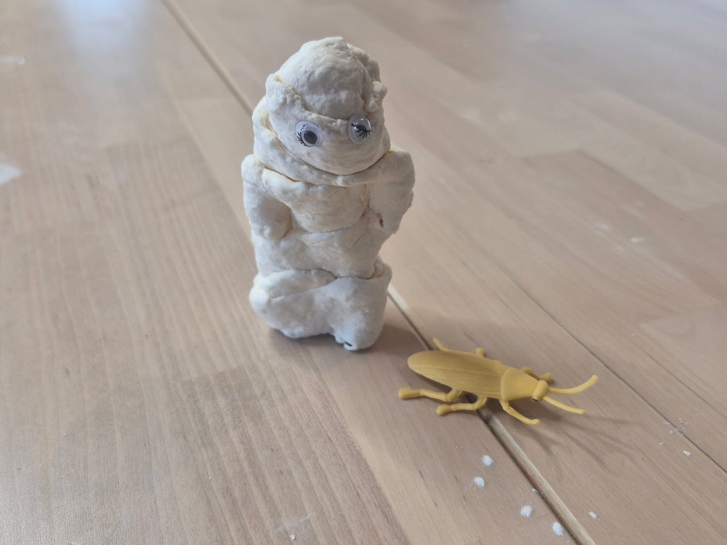 A small white mummy figure sculpted from marshmallow slime, with a plastic beetle at its feet