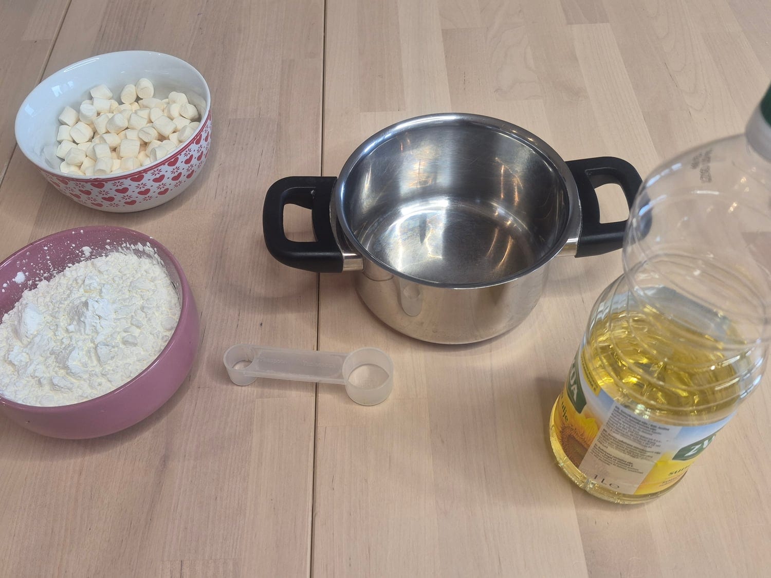 Mummy slime materials: a bowl of mini marshmallows, a bowl of cornstarch, a small pot, a bottle of oil and a measuring spoon