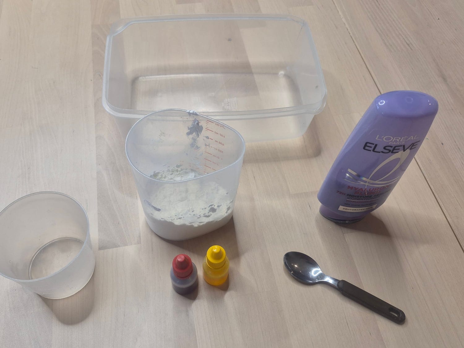 Pumpkin cloud slime materials: a bottle of hair conditioner, a cup of cornstarch, red and yellow food colouring, a spoon and a plastic tub