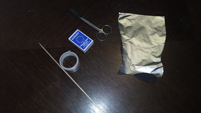 Matches, aluminum foil, a skewer, a paper clip, and tape on a table